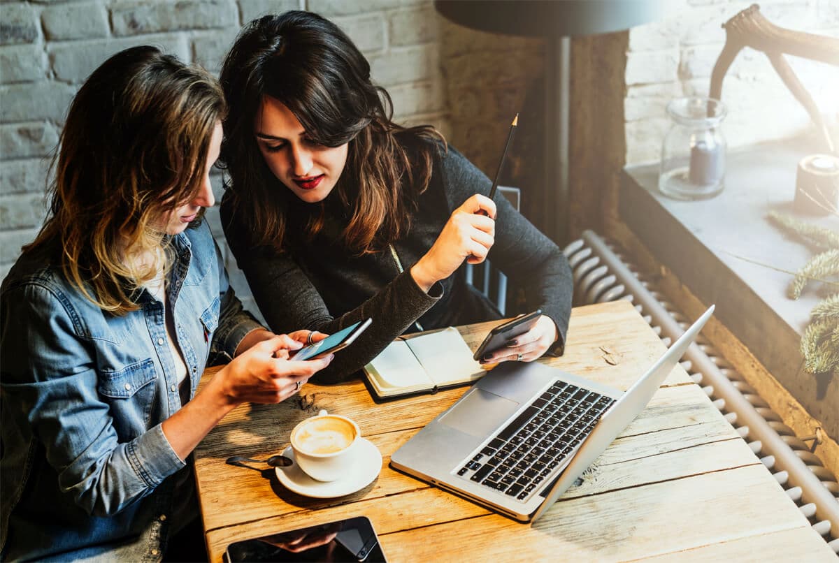 Two women at a cafe conducting a reverse phone search on mobile devices